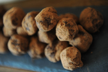 Chocolate truffles in cocoa sprinkled. On the slate board on wooden background. Close-up, texture