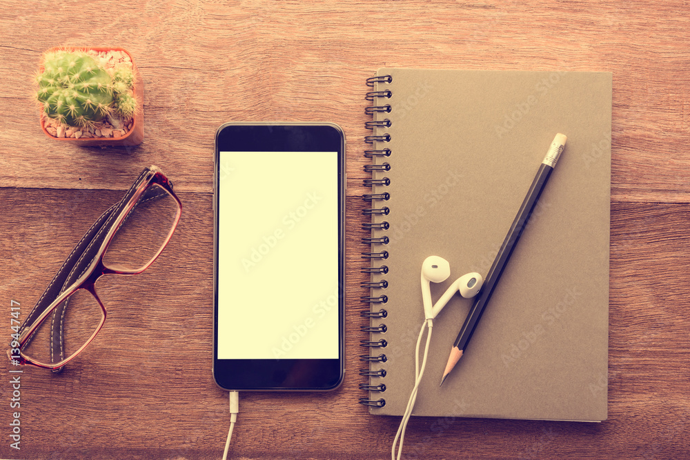 Aufkleber smartphone with white screen and note book on wooden table with copyspace