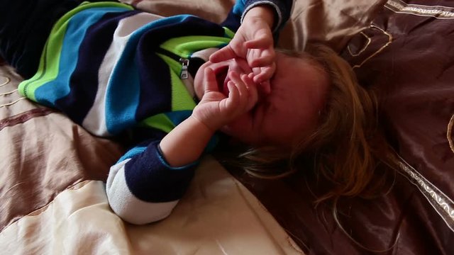 Baby boy is crying on the bed in bedroom before going to bed and calls his mother. Sad toddler is upset and frustrated. Baby tears, tearful child. Lonely boy is crying without his mother