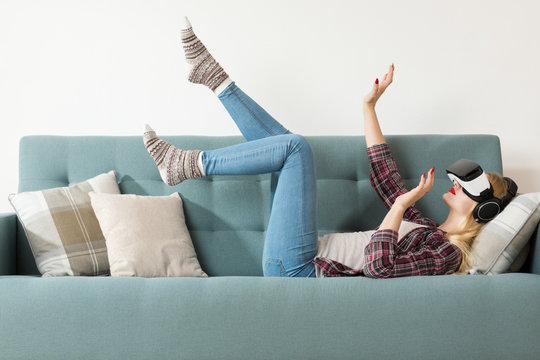 Attractive woman wearing virtual reality glasses lying on a couch. Virtual reality headset. Lifestyle virtual reality concept.