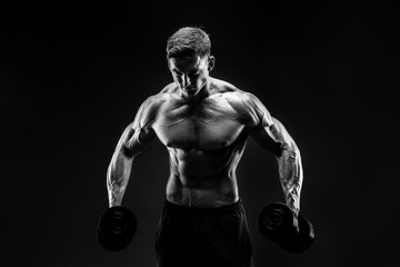 Handsome bodybuilder doing exercise with dumbbell. Studio shot. Black and white photo.