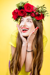 Colorful portrait of a beautiful woman in yellow t-shirt with wreath made of red roses on the yellow background