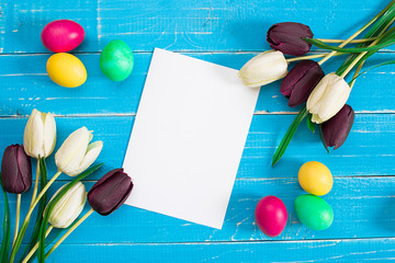 Colorful easter eggs and tulips on blue rustic wooden background