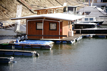 Fototapeta na wymiar Kleines Hausboot aus Holz / Ein kleines Hausboot aus Holz sowie Yachten und Motorboote ankern in einem Binnenhafen am Fluss Rhein.