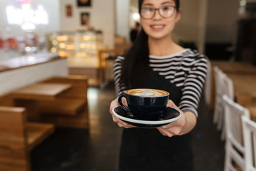 Asian barmaid extends the cup of coffee