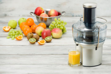 Modern electric juicer, various fruit and glass of freshly made juice, healthy lifestyle concept