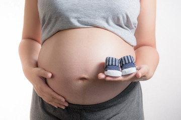 Pregnant woman holding small baby shoes on white background