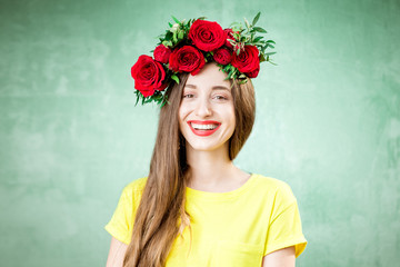 Colorful portrait of a beautiful woman in yellow t-shirt with wreath made of red roses on the green...