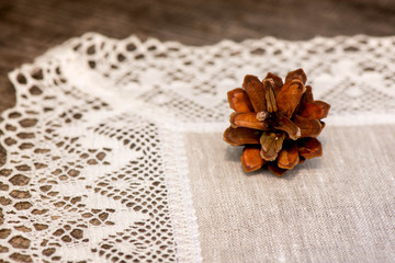 Macro shot of a pine cone on a linen tablecloth with crochet white lace trim on a wooden table

