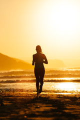 Silhouette of woman running on summer sunset at the beach towards the sun. Healthy exercise and lifestyle.