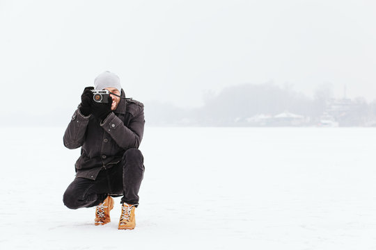 Young man taking a photo on the frozen lake in winter time