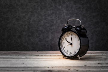 black alarm clock on wooden floor and grey background with free copyspace for yor creativity ideas text