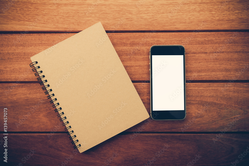 Aufkleber smartphone with white screen and note book on wooden table with copyspace