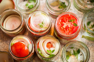 Canning fresh tomatoes with onions for winter in jelly marinade. A shot of basil leaves on top of a red ripe tomato slices and onion rings being put in jar.

