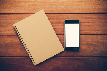 Smartphone with white screen and note book on Wooden Table With Copyspace