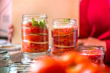 Canning fresh tomatoes with onions for winter in jelly marinade. A shot of basil leaves on top of a red ripe tomato slices and onion rings being put in jar.

