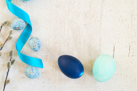 Blue easter eggs and catkins frame on white aged wooden table with copy space