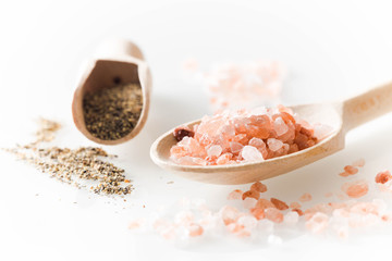 Himalayan salt and pepper on wooden spoon on a white background.