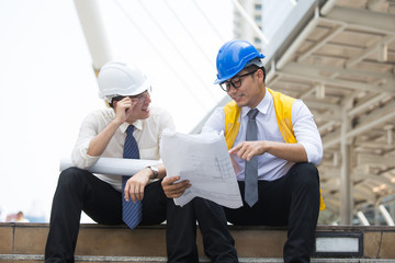 Engineers sitting in front of building with blueprint on hand,Businessman,Engineers reading in blueprint instructions on hand in front of building