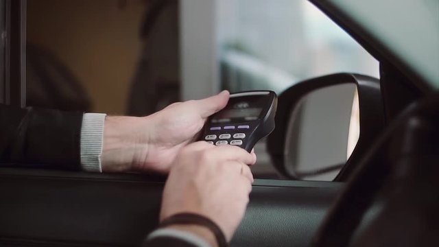 Man paying credit card for buying inside car, enters a PIN code. Close-up view of businessman hand from the car window.