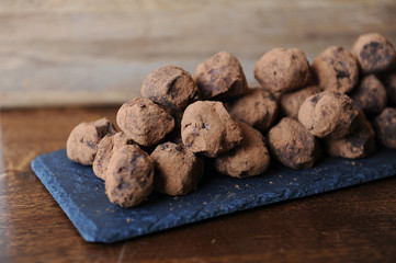 Chocolate truffles in cocoa sprinkled. On the slate board on wooden background. Close-up, texture