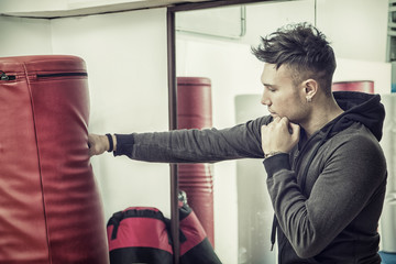 Handsome young man in gym next to punching bag, wearing training suit