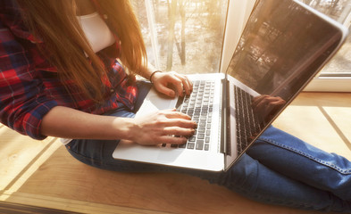 The young woman is sitting on the windowsill and working at laptop