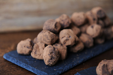 Chocolate truffles in cocoa sprinkled. On the slate board on wooden background. Free space for design