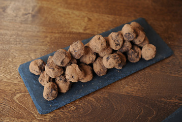 Chocolate truffles in cocoa sprinkled. On the slate board on wooden background. Free space for design