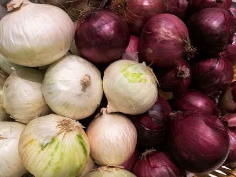 Fresh organic white onion bulbs and red shallot among many onion and shallot background in the basket in supermarket. Heap of onion root. Close-up red onion shallot texture