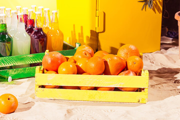 Orange wood box and lemonade bottles in summer sunny time on beach of ocean with palm leaves useful for background