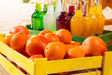 Orange wood box and lemonade bottles in summer sunny time on beach of ocean with palm leaves useful for background