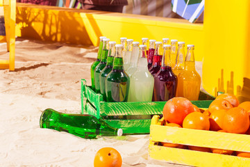Orange wood box and lemonade bottles in summer sunny time on beach of ocean with palm leaves useful for background