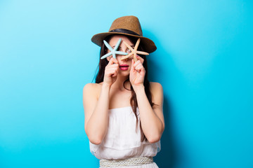 beautiful surprised young woman with starfishes standing in front of wonderful blue background