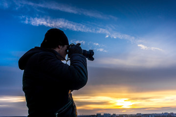 Photographer takes shot of sunset at background of clourful dramatic sky