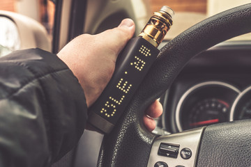 Mans hand on steering wheel of car with modern vaping device or vaporizer