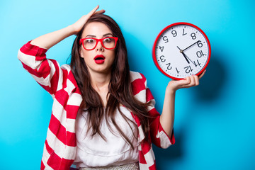 beautiful surprised young woman with clock standing in front of wonderful blue background