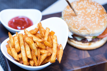 French fries on white plate with ketchup and burger. Focus on fries