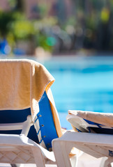 Beach towel in cream color hung on the empty deck chair by the swimming pool