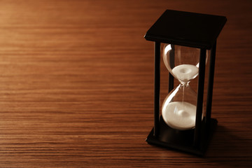 Black hourglass with white sand on wooden background