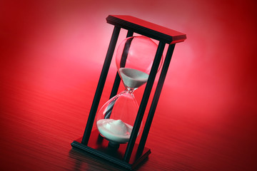 Black hourglass with white sand on red background