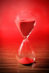 Crystal hourglass with red sand on wooden table