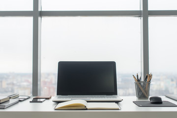 Workplace with notebook laptop Comfortable work table in office windows and city view.