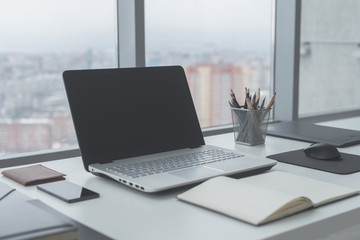 Fototapeta premium Workplace with notebook laptop Comfortable work table in office windows and city view.