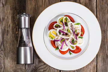 Salad with squid, egg and tomato on white plate on background of