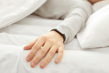 Fototapeta na wymiar Hand of young man with sleep tracker resting in bed at home