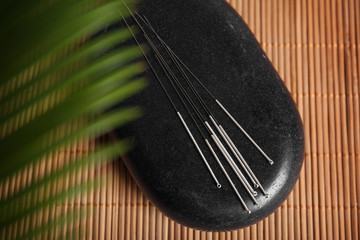 Black pebble with set of acupuncture needles on bamboo mat