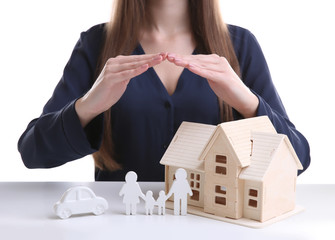 Woman holding hands under model of house, car and family on white table