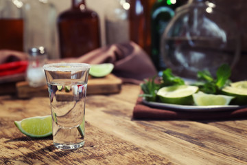 Tequila shot with juicy lime and salt on wooden table