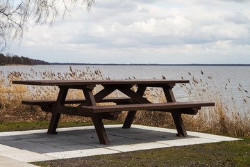 Fototapeta na wymiar Hölzerne Sitzbank mit Tisch am Ufer eines Binnensee